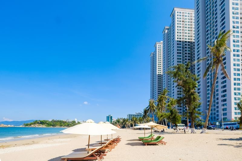 Hon Chong beach with white parasols and palm trees in front of the Sunrise Apartment towers, Nha Trang