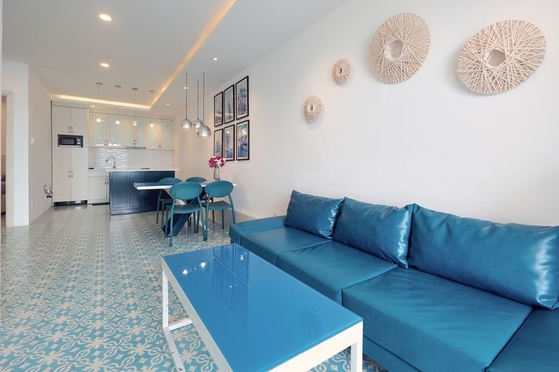 Open-plan living room with teal leather sofa and kitchen behind